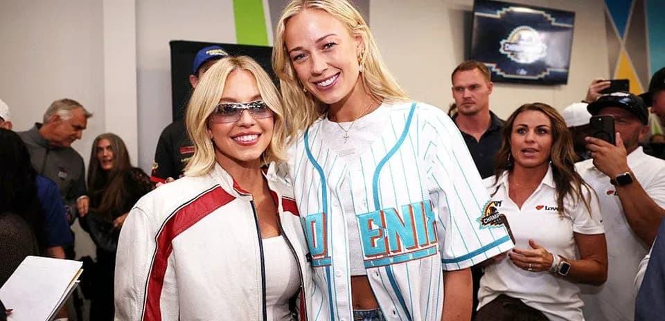 Dos mujeres posando en evento con público detrás