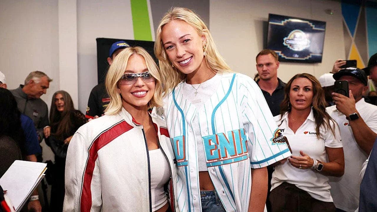 Dos mujeres posando en evento con público detrás