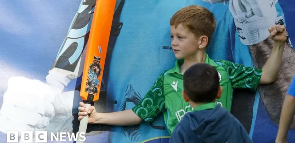 Niño sosteniendo un bate de cricket frente a un cartel