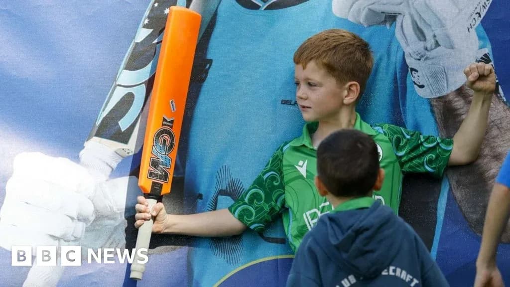 Niño sosteniendo un bate de cricket frente a un cartel