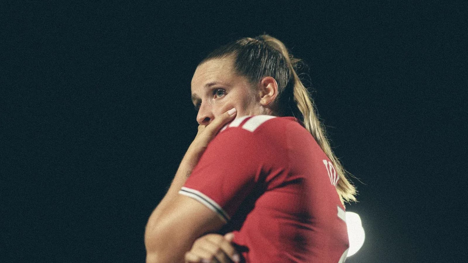 Jugadora con camiseta roja pensativa en el campo