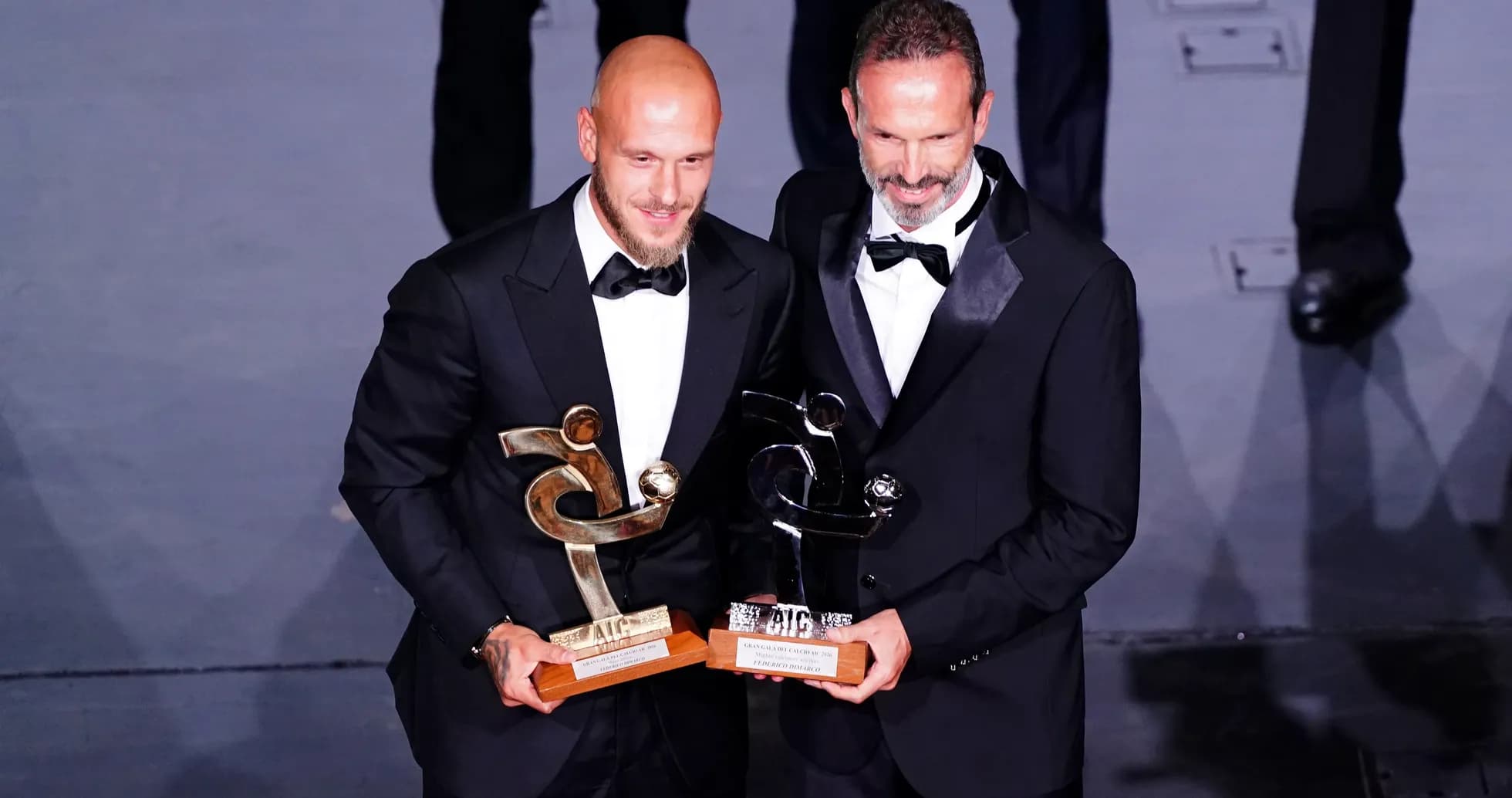 Dos hombres en traje sosteniendo trofeos en evento