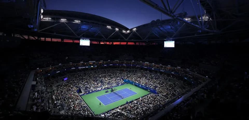 Estadio lleno durante partido de tenis al anochecer