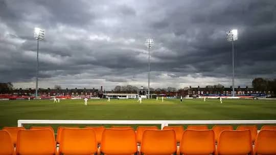 Campo de cricket bajo nubes oscuras y luces encendidas
